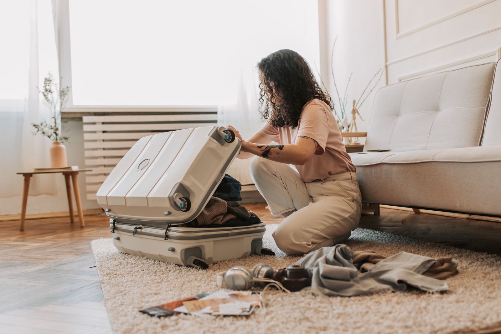 Packing for a fresh start A woman kneeling on a living room rug, packing an open suitcase with folded clothes for a solo trip